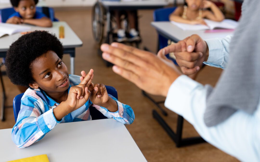 Diverse male teacher teaching school boy using sign language in class at elementary school. School, disability and education, unaltered.