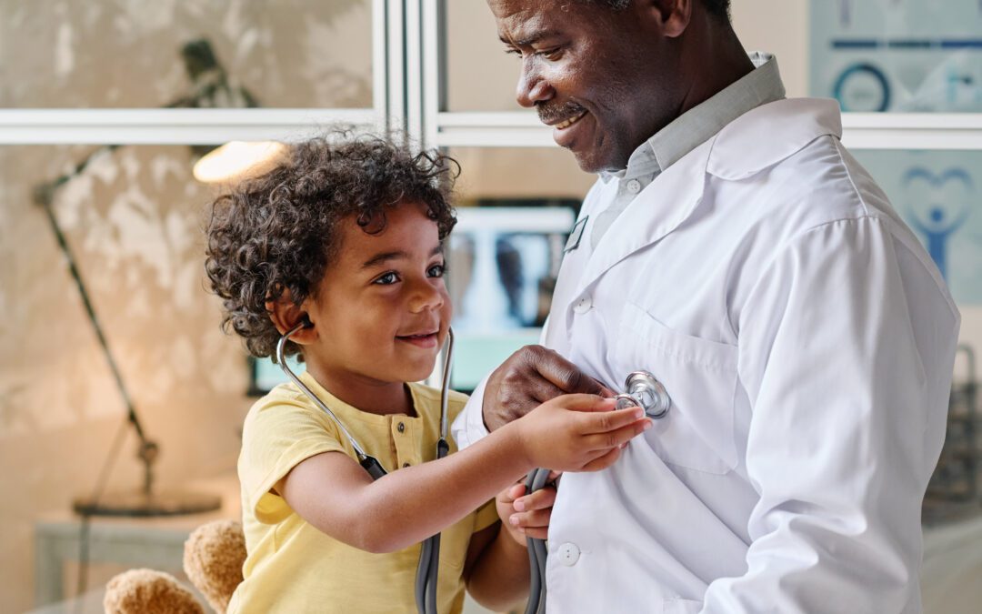 African little boy playing with stethoscope together with doctor during medical exam at office