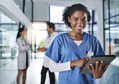 Shot of a young doctor using a digital tablet in a hospital with her colleagues in the background.